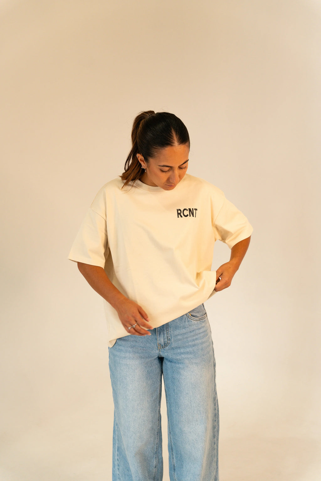 Woman wearing beige RCNT t-shirt and light blue jeans against plain beige background