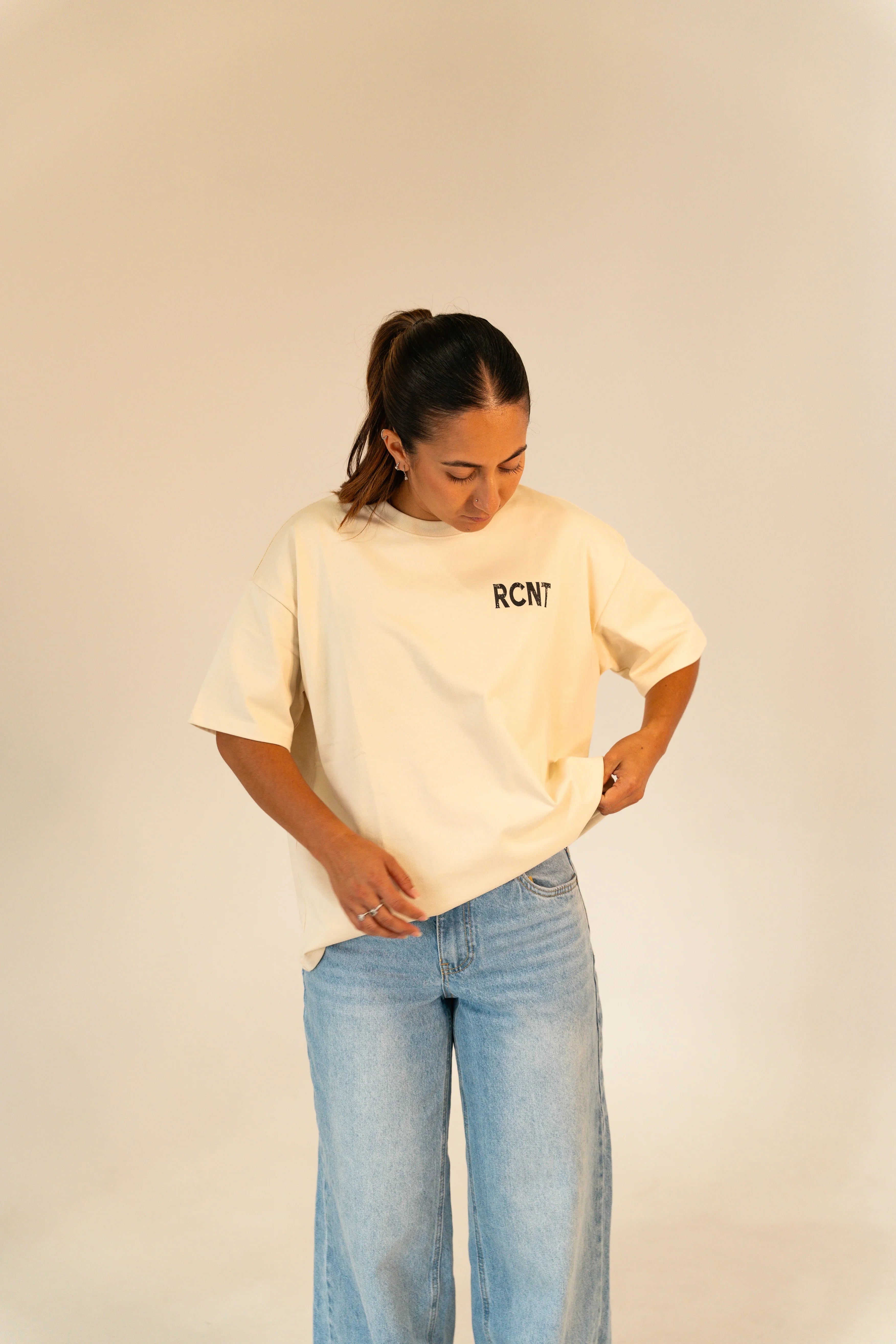 Woman wearing beige RCNT t-shirt and light blue jeans against plain beige background