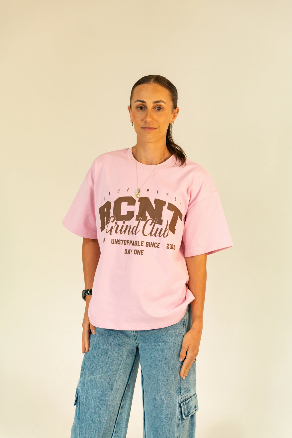 Woman wearing pink RCNT Grind Club t-shirt and blue cargo jeans against light background