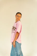 Woman in pink graphic t-shirt and blue denim cargo pants standing against beige background