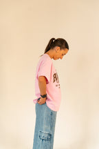 Woman in pink graphic t-shirt and blue cargo jeans standing against beige background