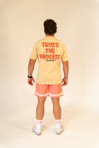 Man wearing beige T-shirt with 'Trust The Process' text and coral shorts in studio