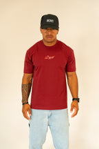 Man wearing maroon RCNT T-shirt and black RCNT cap with light blue jeans on beige background
