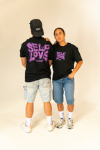 Two models wearing black self love graphic t-shirts with purple text, denim shorts, and white sneakers in studio