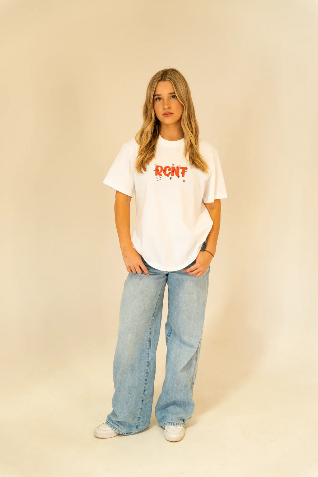 Young woman in casual white RCNT graphic t-shirt and wide-leg light blue jeans posing in studio