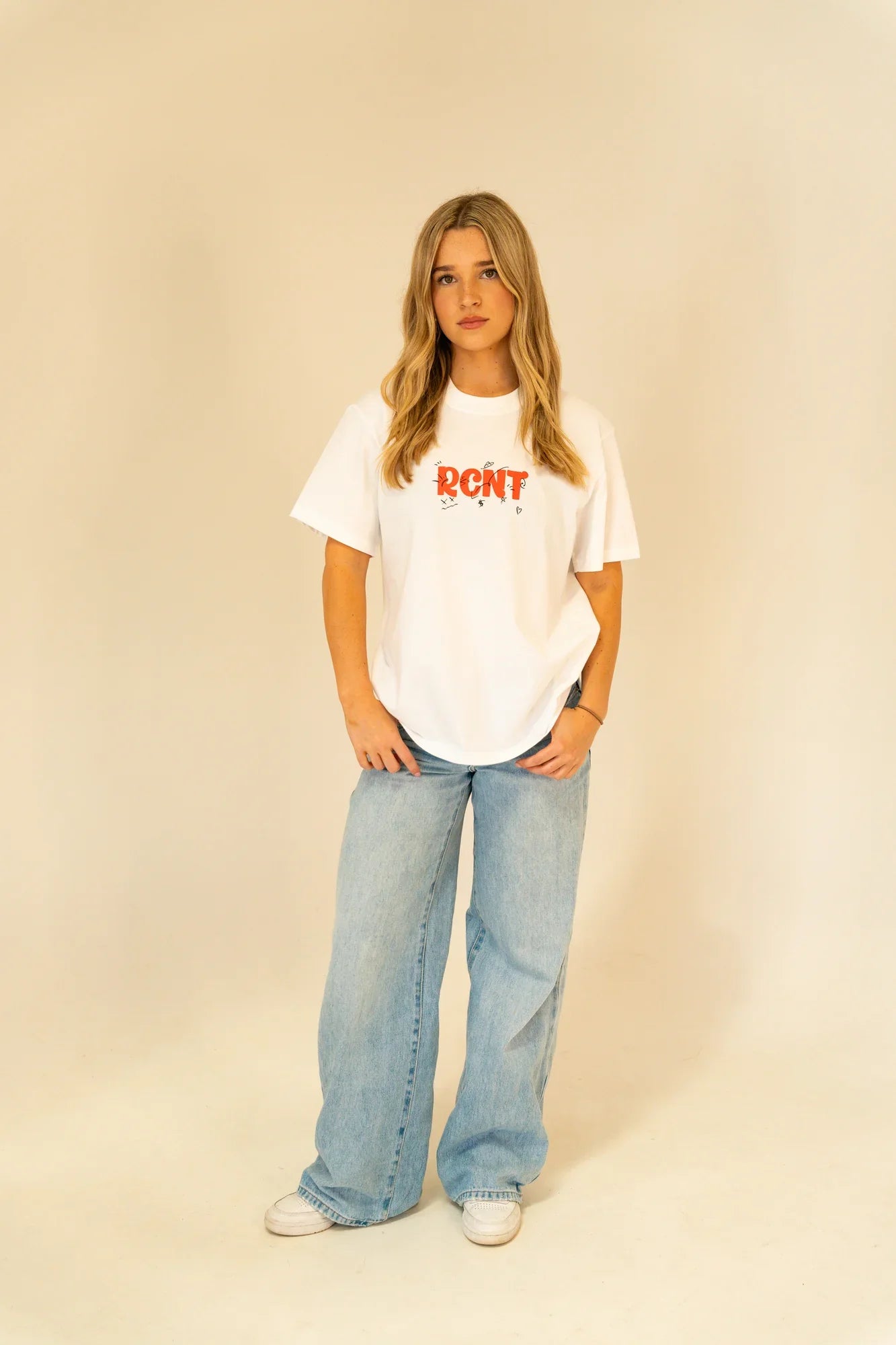 Young woman in casual white RCNT graphic t-shirt and wide-leg light blue jeans posing in studio