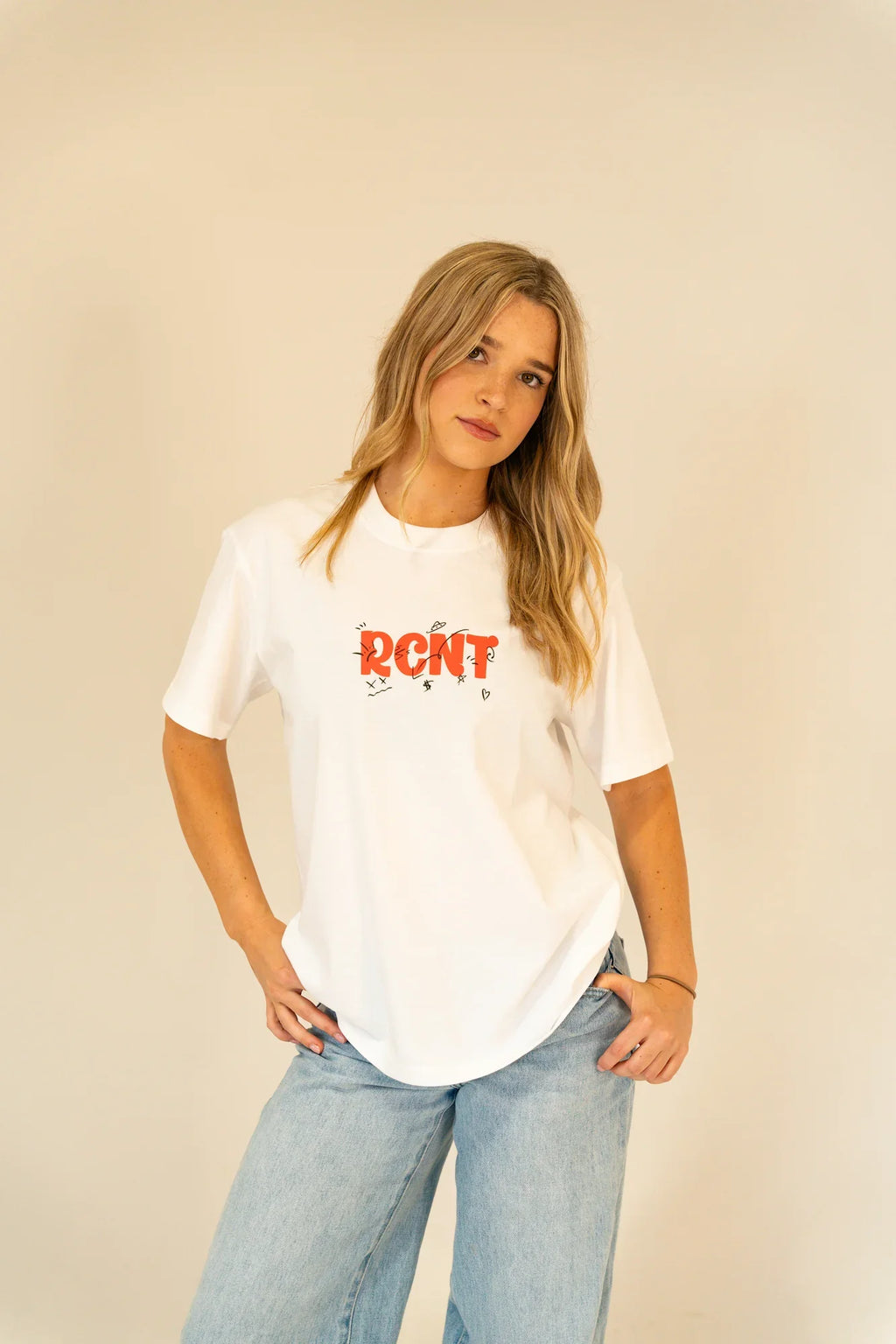 Young woman wearing white RCNT graphic t-shirt and light blue jeans against beige background