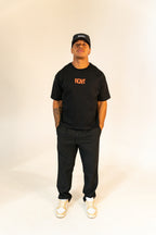 Man wearing black RCNT cap and black t-shirt with orange RCNT logo, black pants, white sneakers