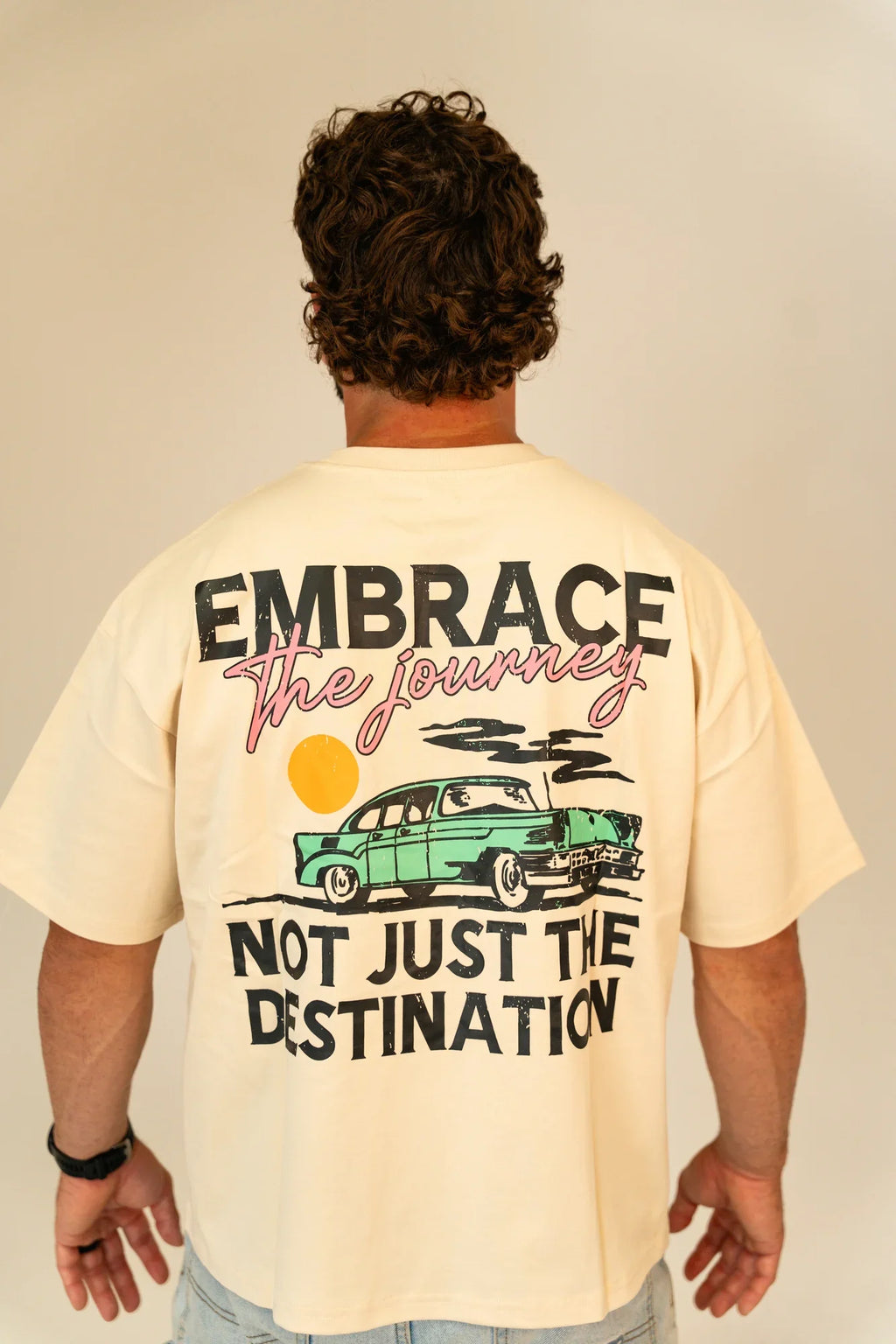Man wearing cream t-shirt with vintage car and quote Embrace the journey, not just the destination
