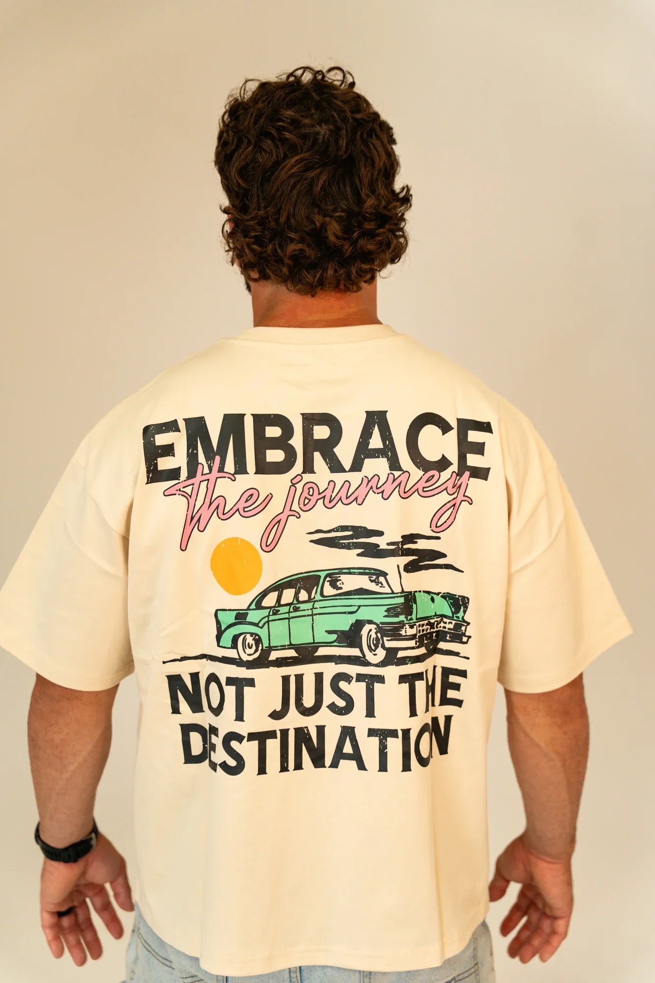 Man wearing cream t-shirt with vintage car and quote Embrace the journey, not just the destination