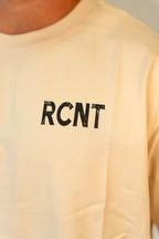 Close-up of beige t-shirt with black distressed RCNT logo printed on chest