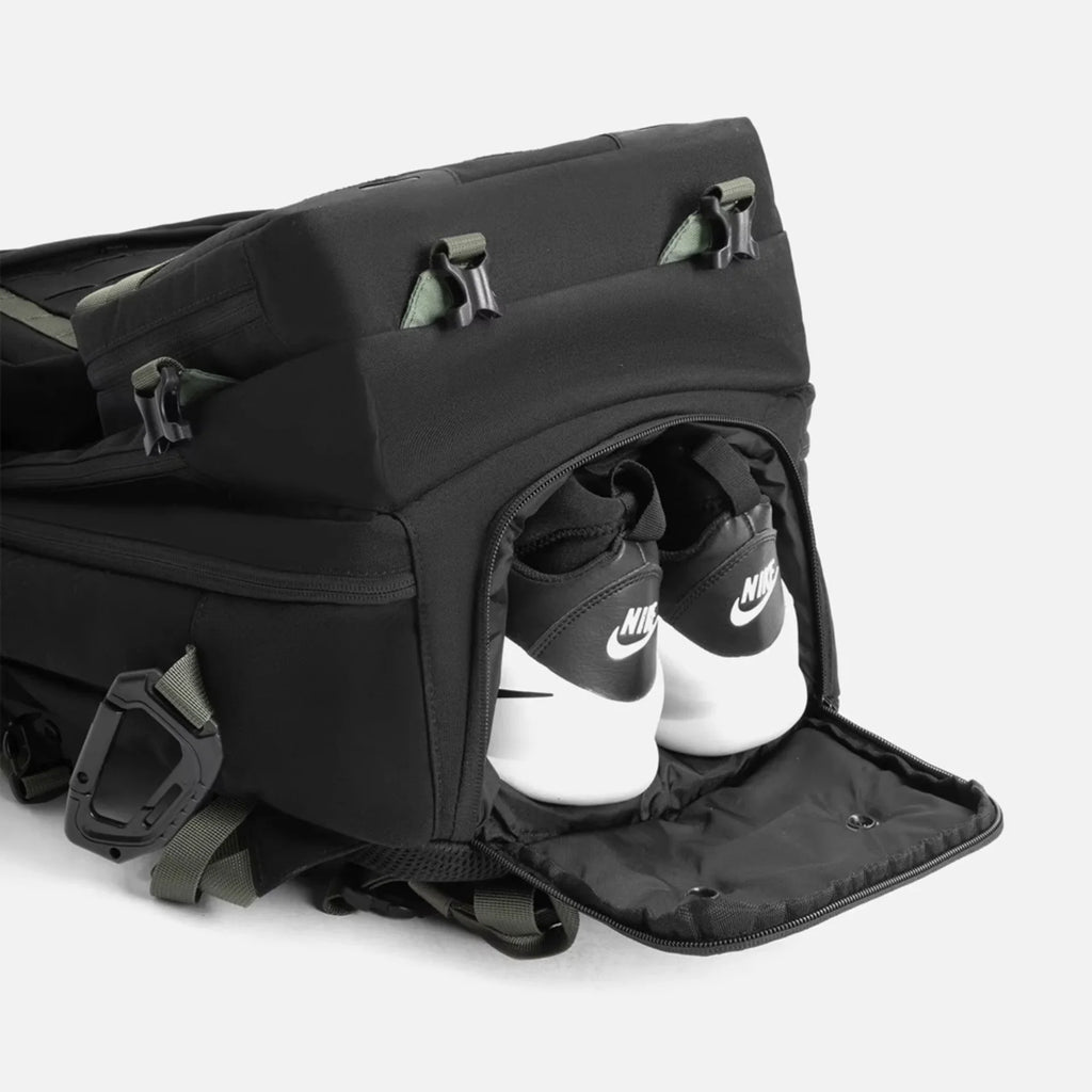 Black backpack with a zippered shoe compartment revealing white and black Nike sneakers stored inside