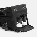Black backpack with a zippered shoe compartment revealing white and black Nike sneakers stored inside