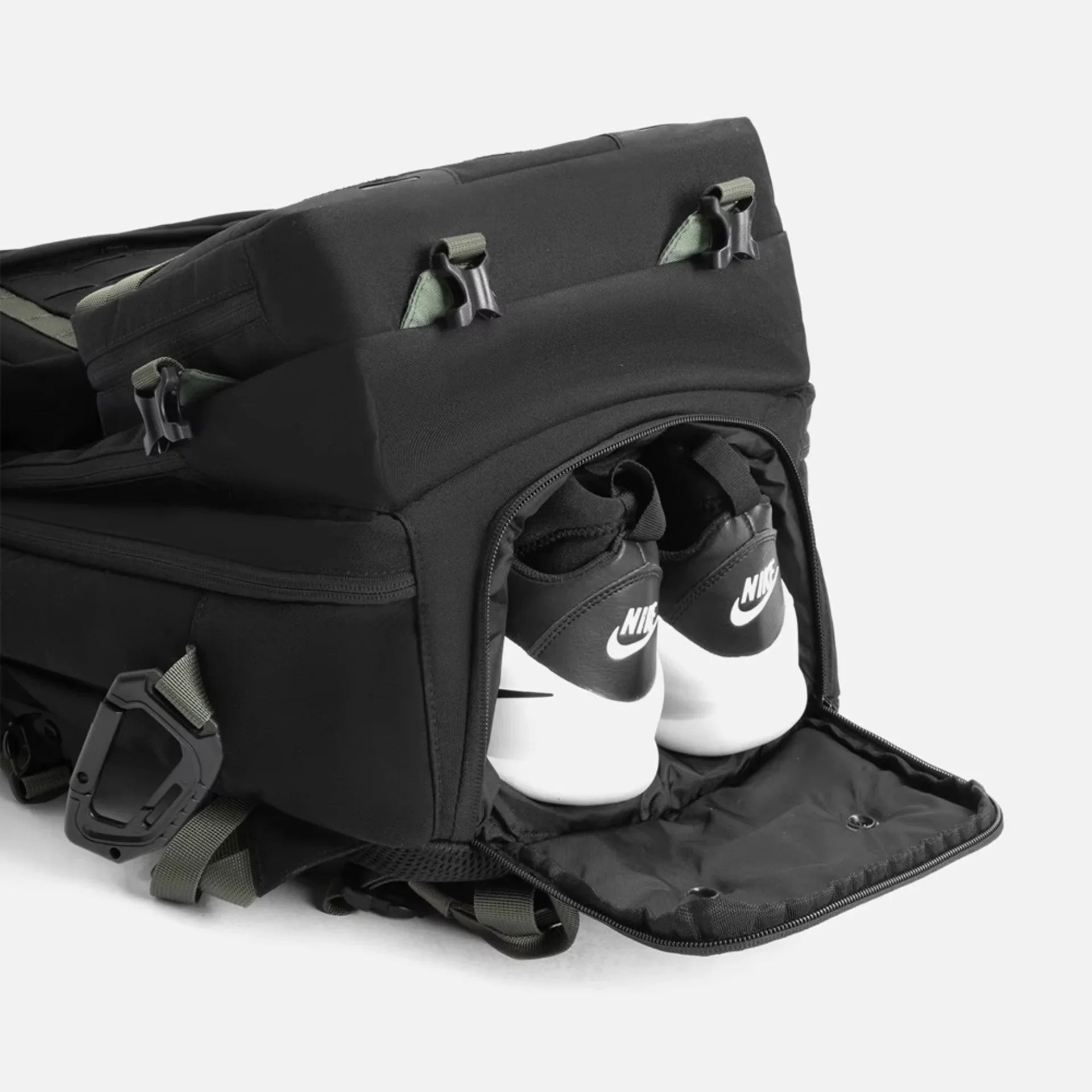 Black backpack with a zippered shoe compartment revealing white and black Nike sneakers stored inside