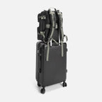 Black backpack secured with straps on top of black hard-shell suitcase with wheels on white background