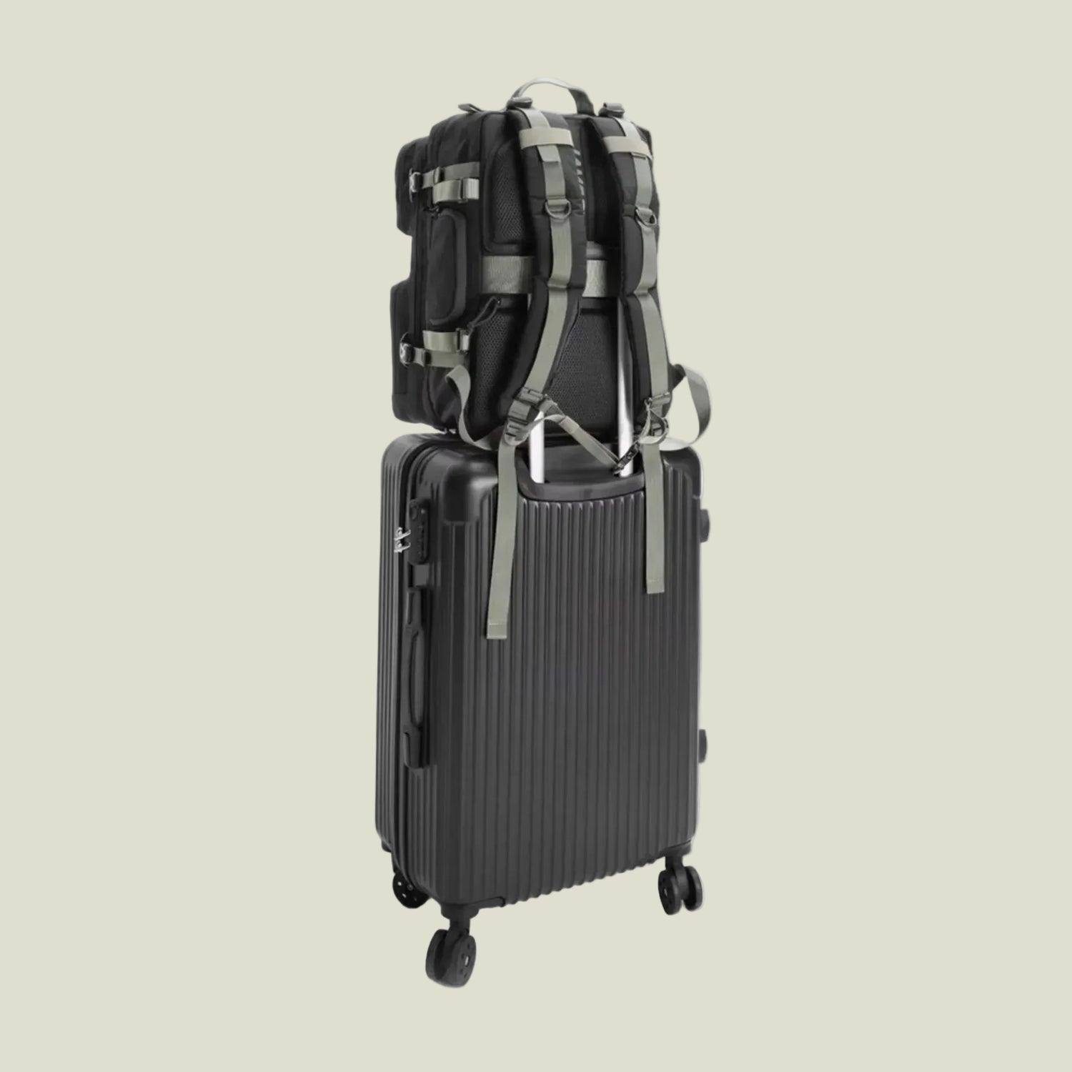 Black backpack secured with straps on top of black hard-shell suitcase with wheels on white background