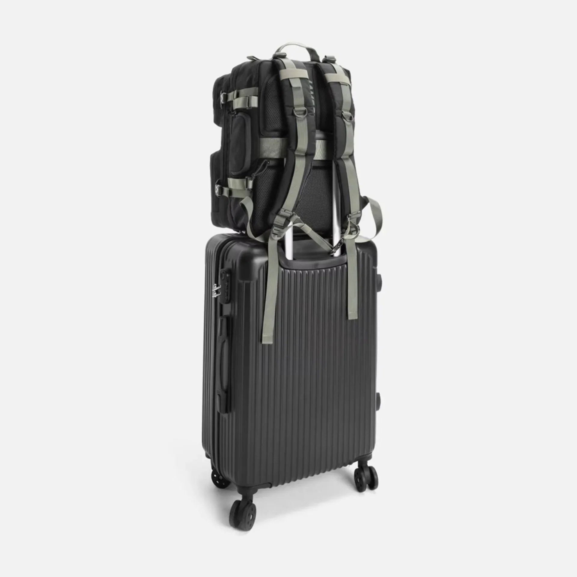 Black backpack secured with straps on top of black hard-shell suitcase with wheels on white background