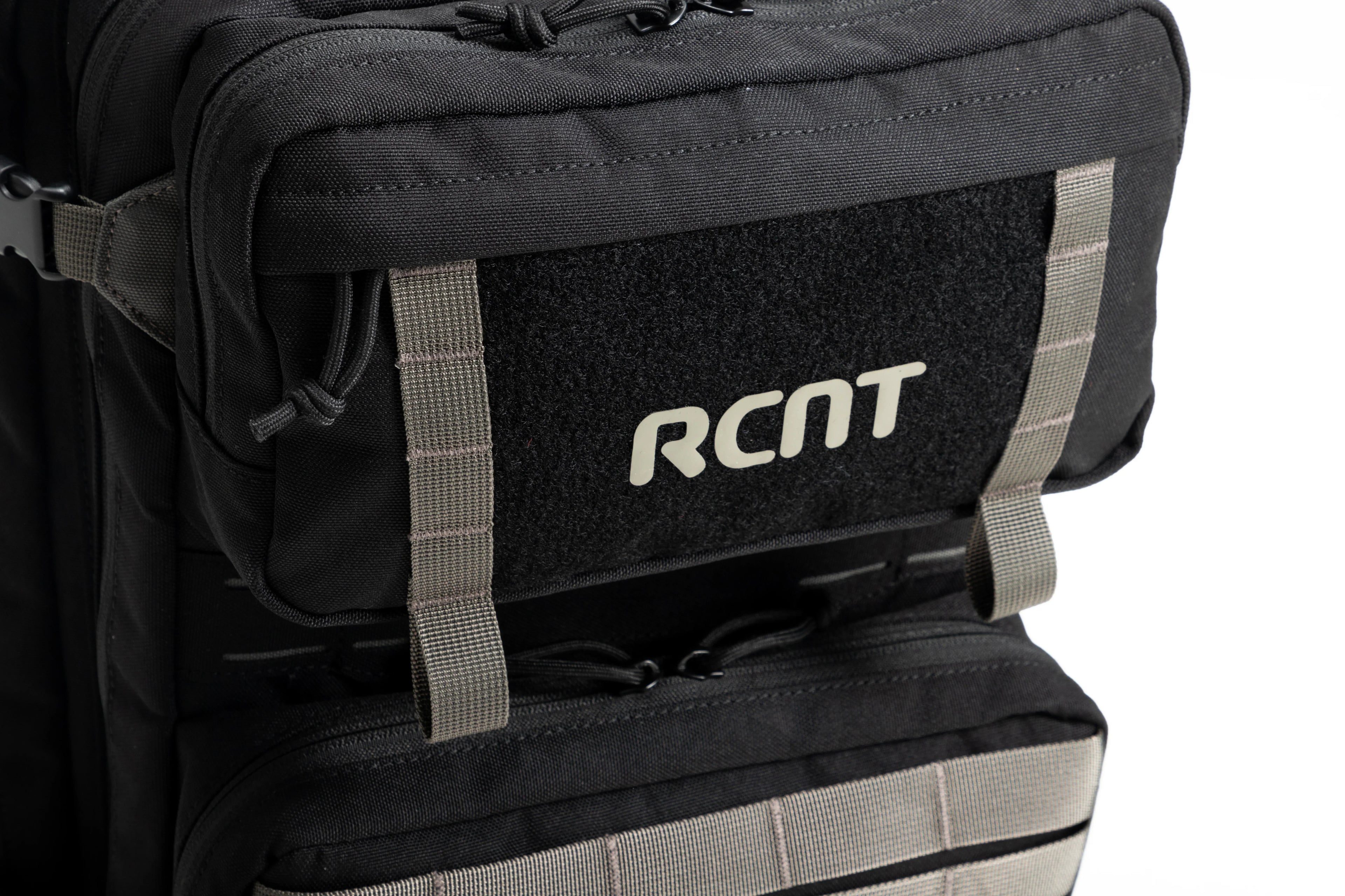 Close-up of black RCNT branded tactical backpack front pocket with gray straps and zipper pulls