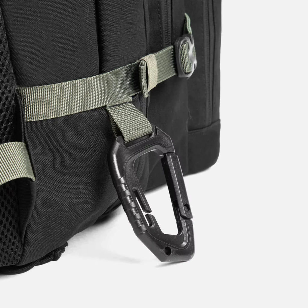 Black backpack with green straps and attached black carabiner clip close-up