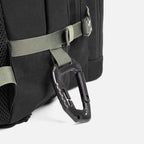 Black backpack with green straps and attached black carabiner clip close-up