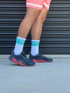 Person wearing black and pink sneakers with white socks and coral shorts standing on concrete