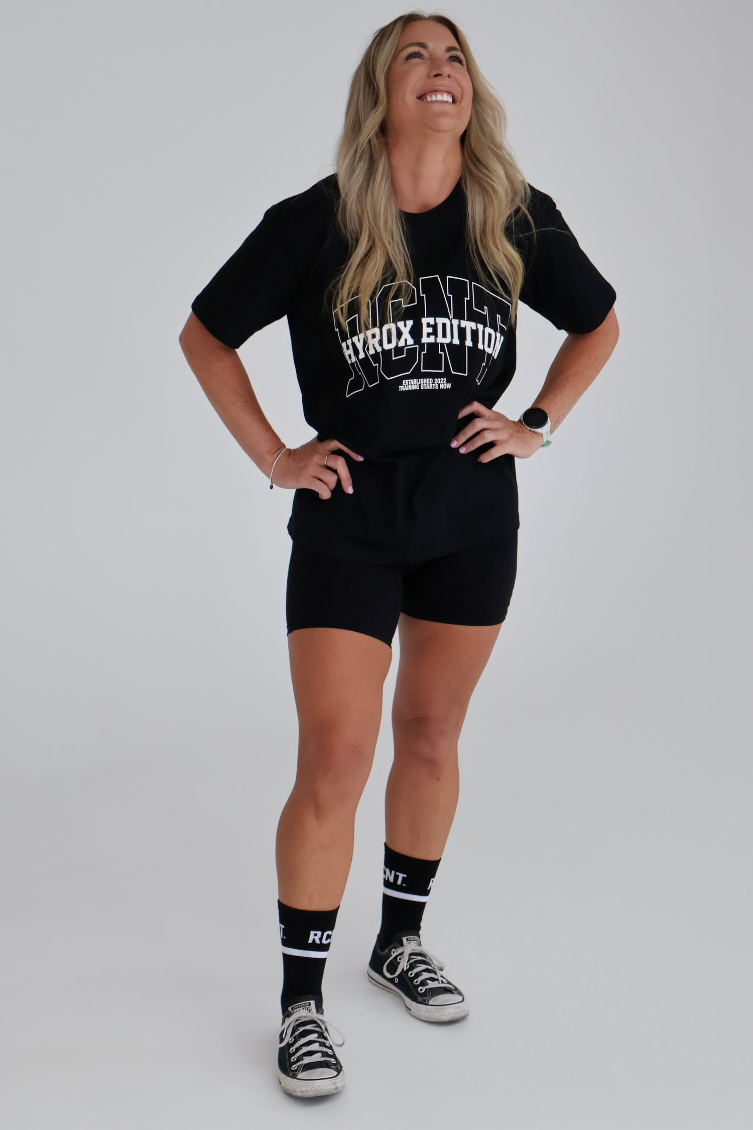 Woman wearing a black t-shirt, shorts, and socks with text on a plain background