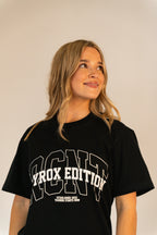 Young woman with blonde hair wearing black Hyrox Edition T-shirt standing against plain background