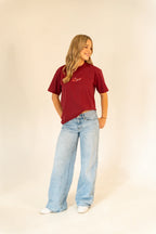 Young woman in maroon graphic t-shirt and wide-leg light blue jeans standing on beige background