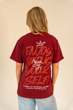 Person wearing maroon t-shirt with motivational prints 'Enjoy being yourself' and 'Never give up' on back