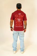 Man wearing maroon graphic t-shirt with motivational text, light blue jeans, black cap, and Nike sneakers