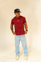 Man in a red RCNT t-shirt, light blue jeans, black RCNT cap, and beige sneakers on white background