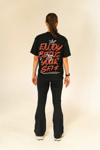 Woman with ponytail wearing black graphic t-shirt and flared pants on beige background