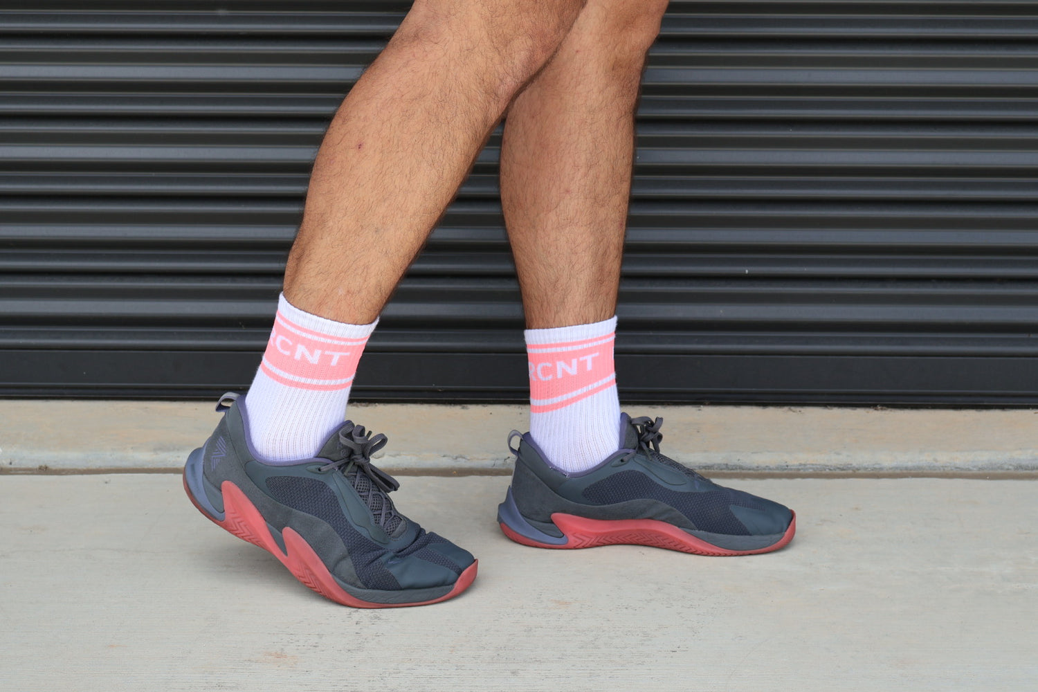 Person wearing pink and white athletic socks with 'RCNT' text, navy sneakers, standing outdoors