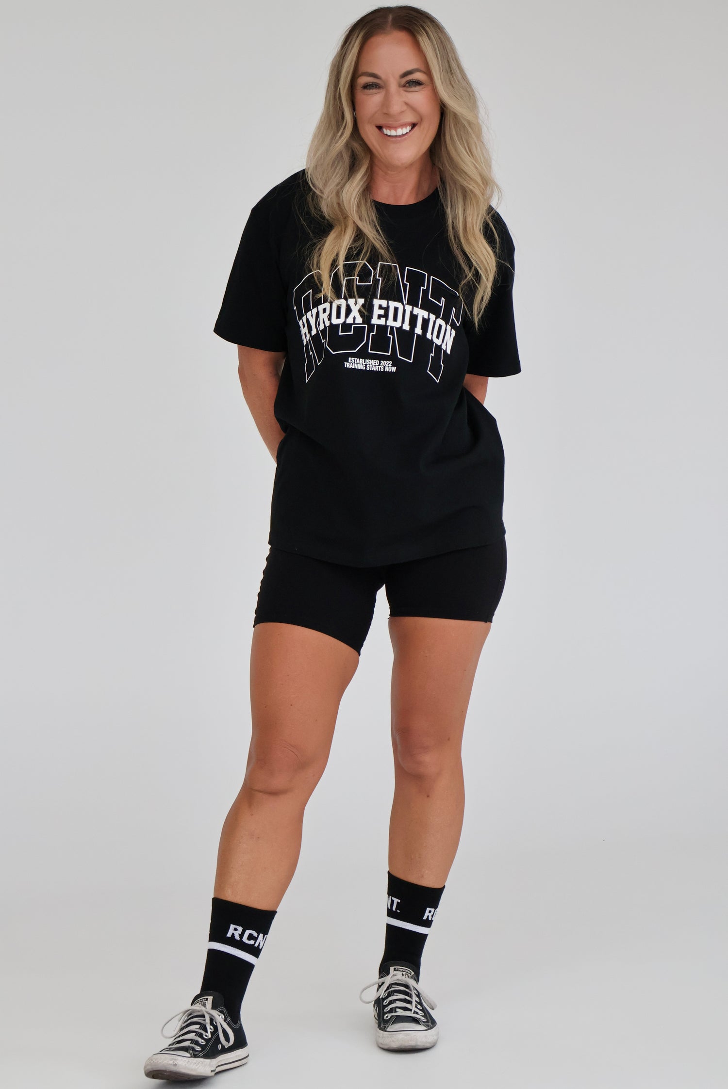 Woman in black HYROX EDITION t-shirt, black shorts, and RCNT socks, casual athletic style