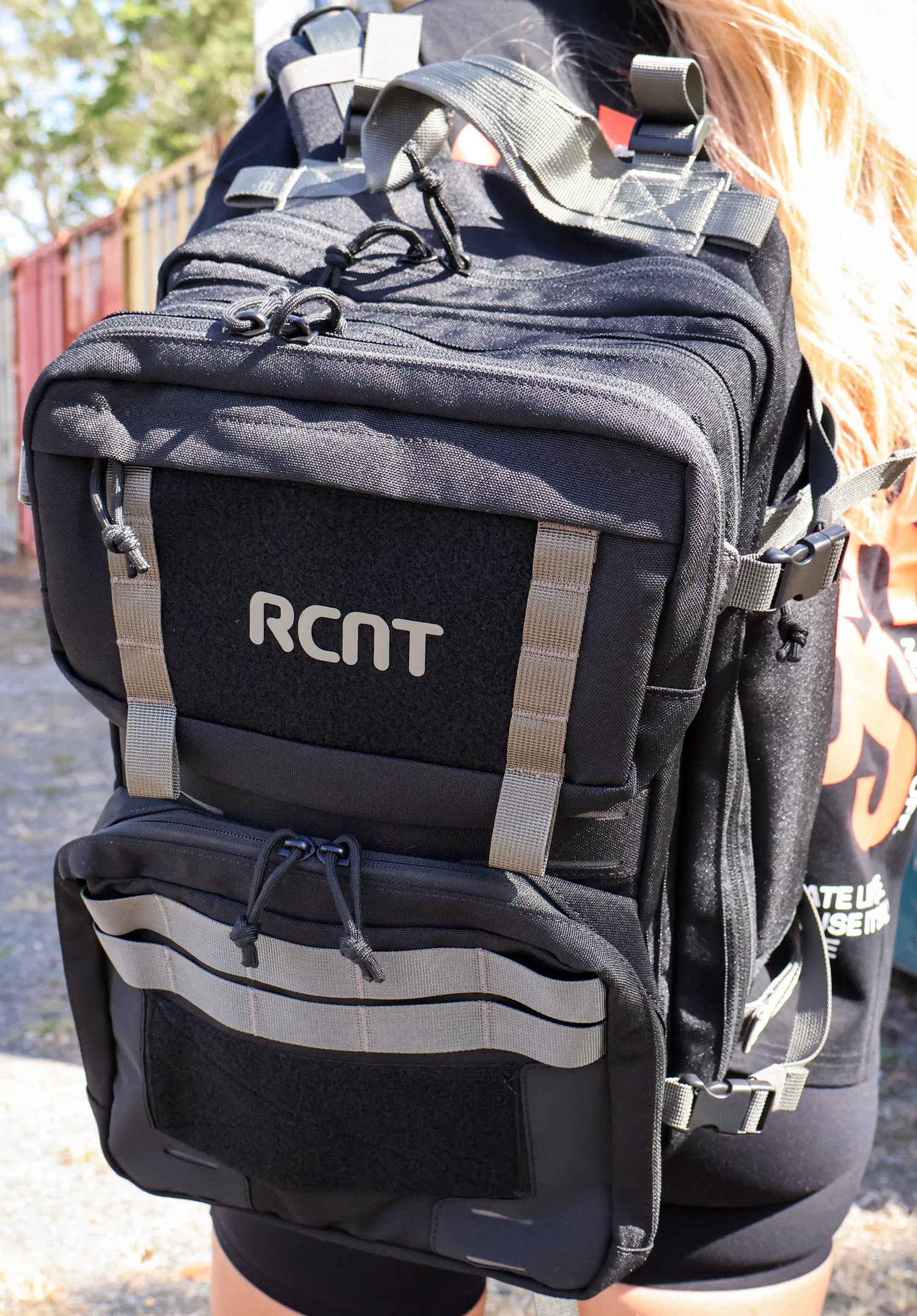 Black tactical backpack with RCNT logo, worn outdoors, featuring multiple pockets and straps