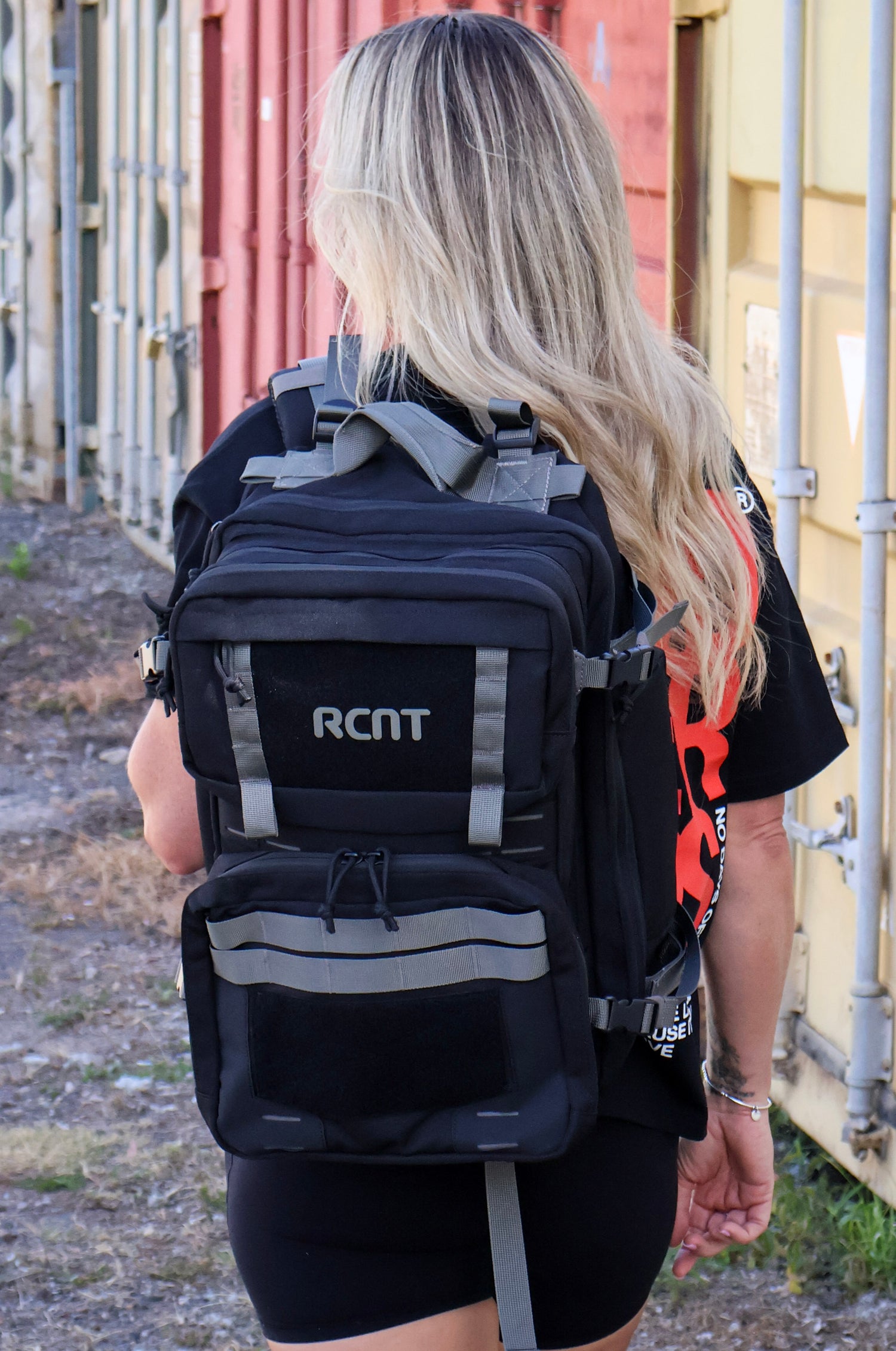 Woman outdoors wearing black RCNT tactical backpack and black athletic outfit