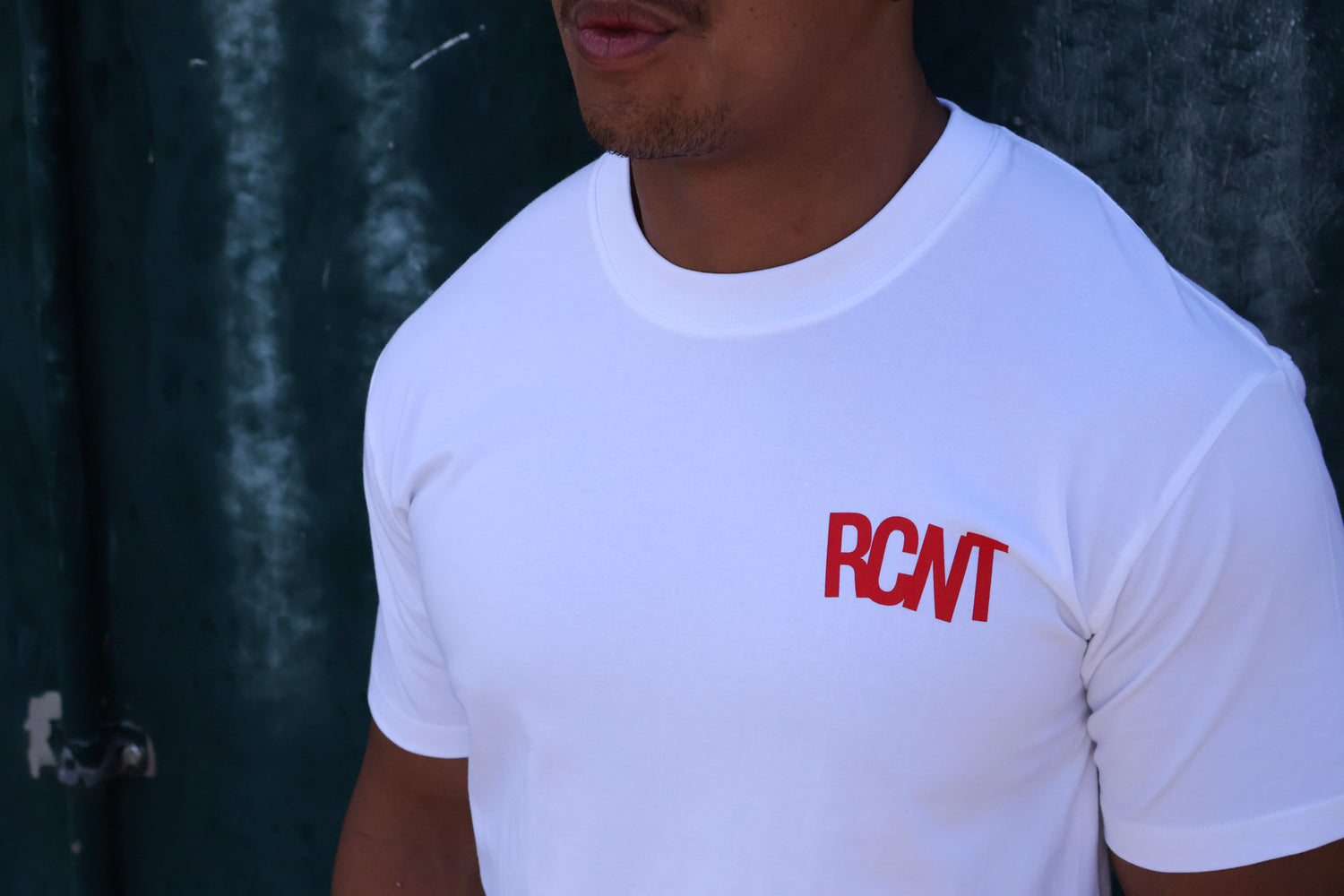 Man wearing white crew neck t-shirt with red RCNT logo, casual streetwear style