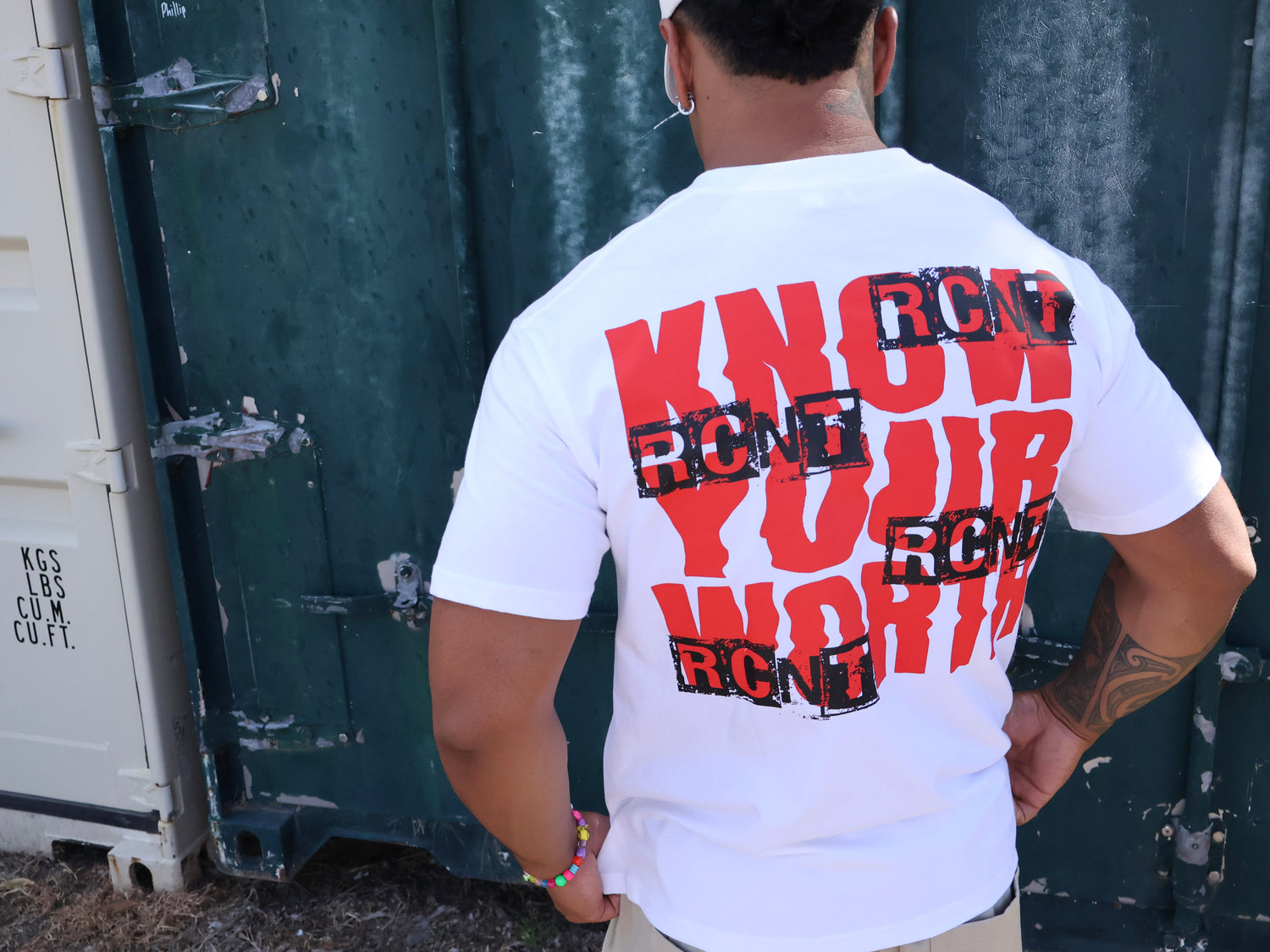 Man wearing white graphic t-shirt with bold red 'Know Your Worth' and black RCNT text print.
