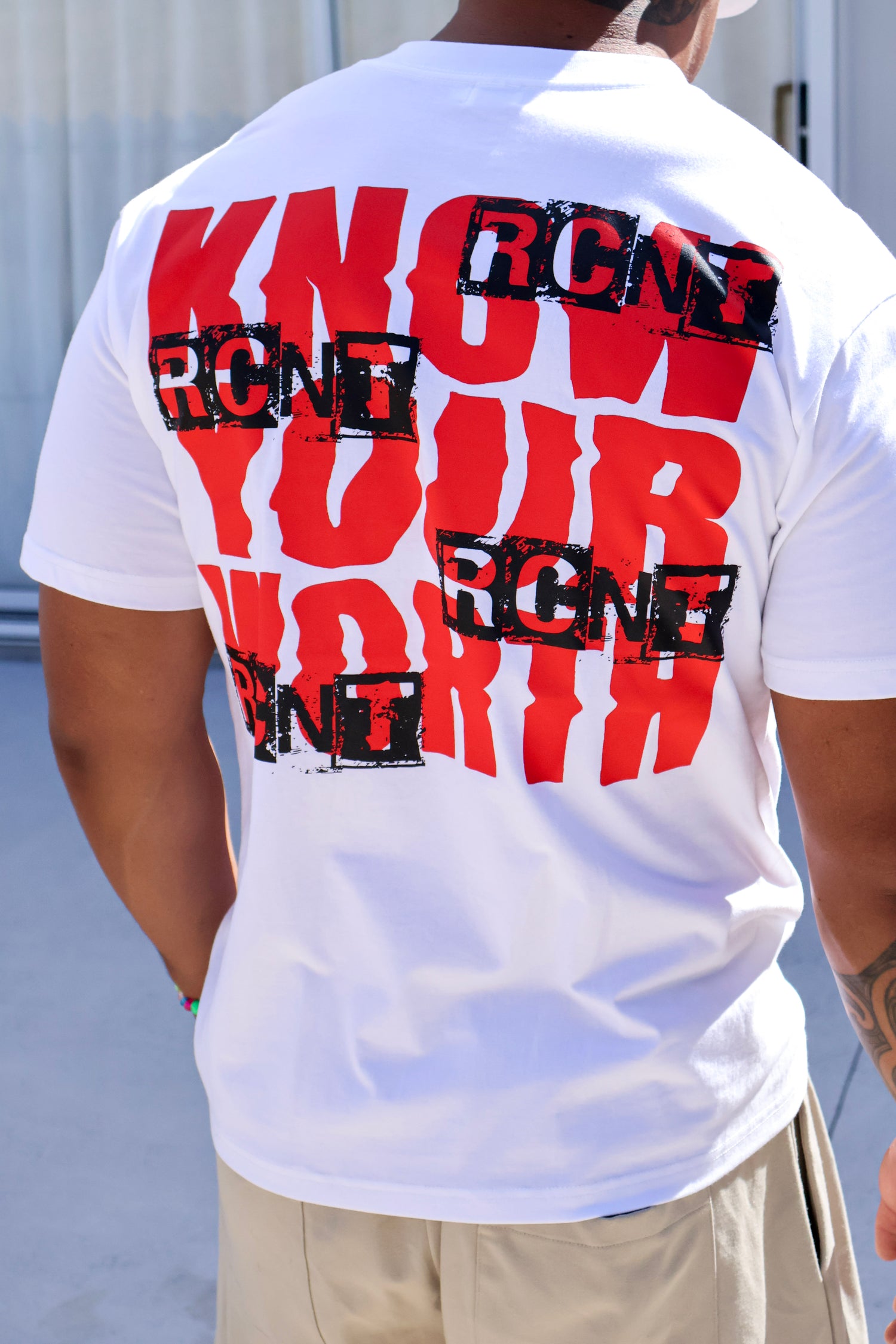 Person wearing white t-shirt with bold red 'KNOW YOUR WORTH' and black RCNT graphic print