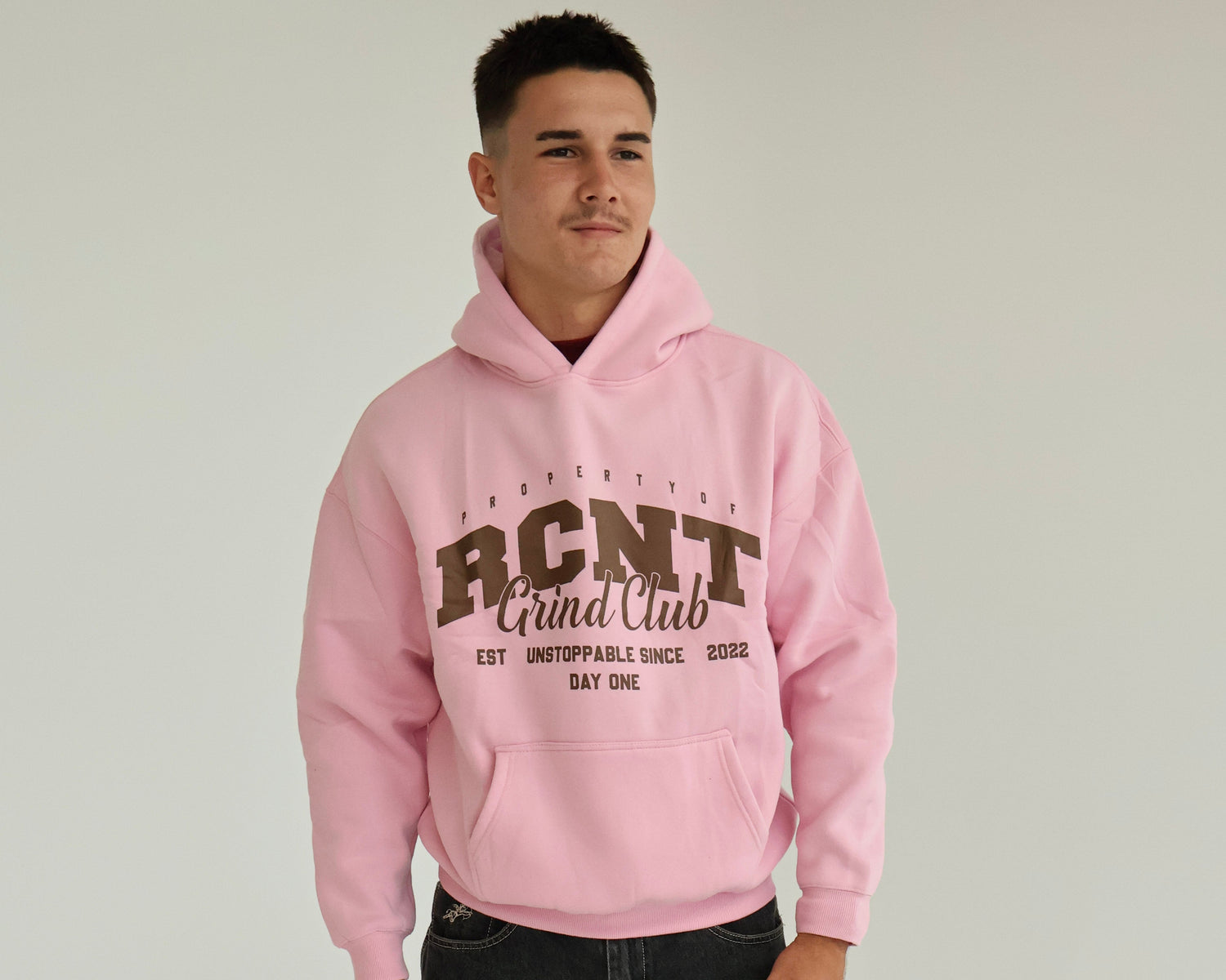 Person wearing a pink hoodie with 'BCNT' text on a plain background