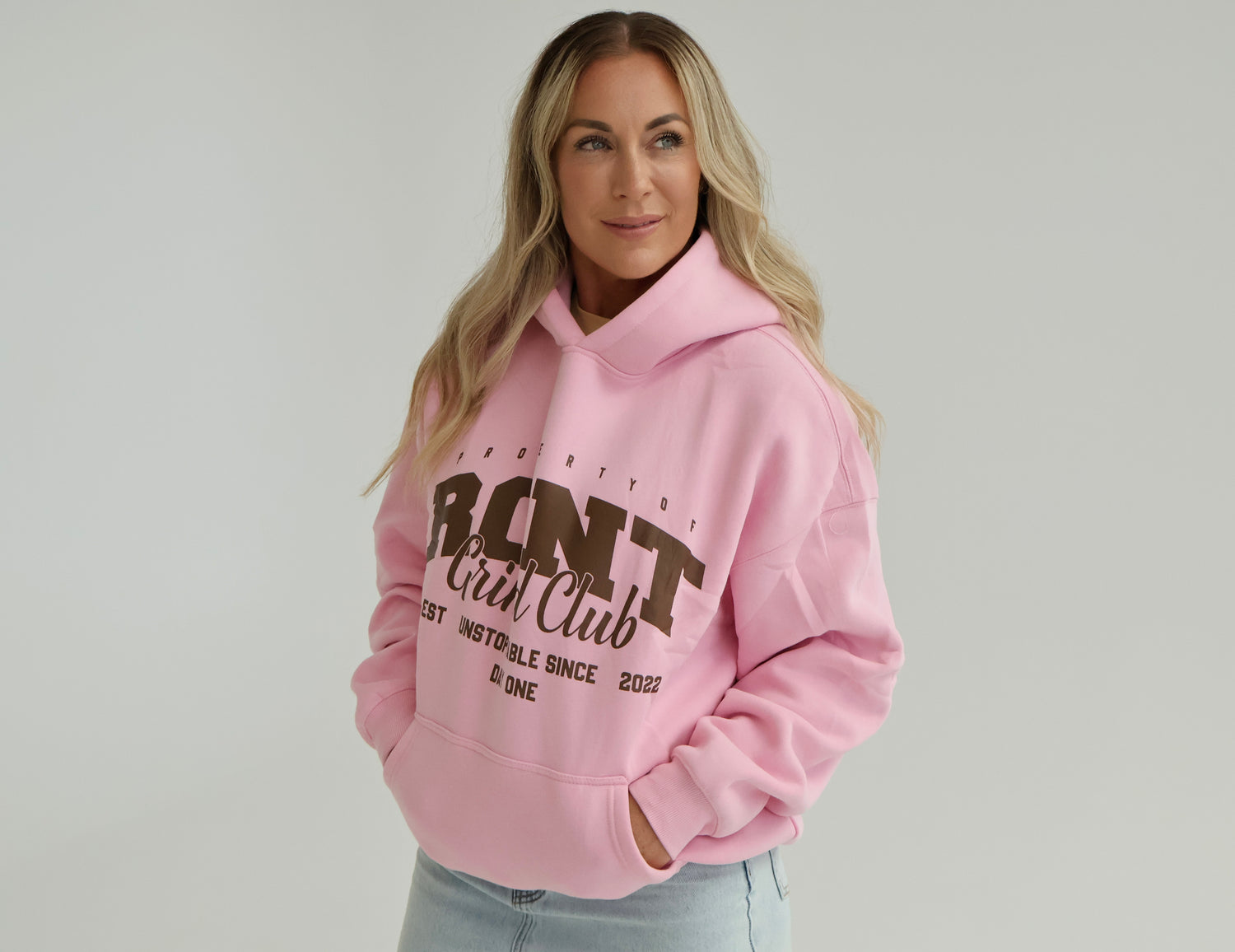 Woman wearing a pink hooded sweatshirt with bold text, styled with light jeans, in studio