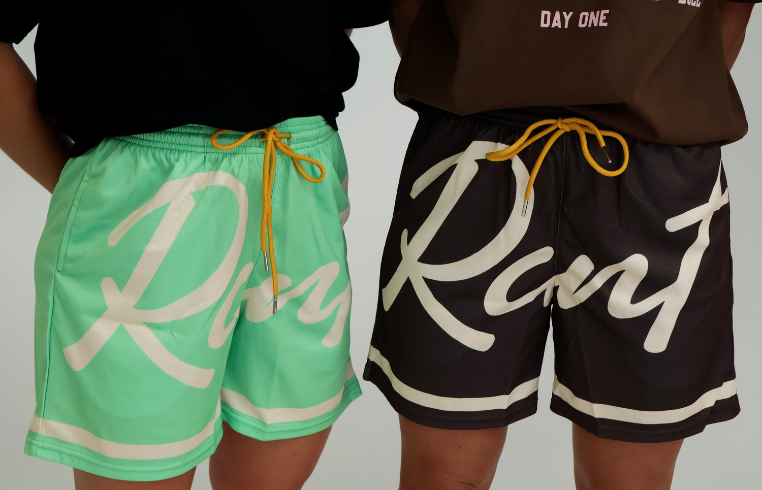 Two people wearing mint green and black athletic shorts with bold script lettering and yellow drawstrings
