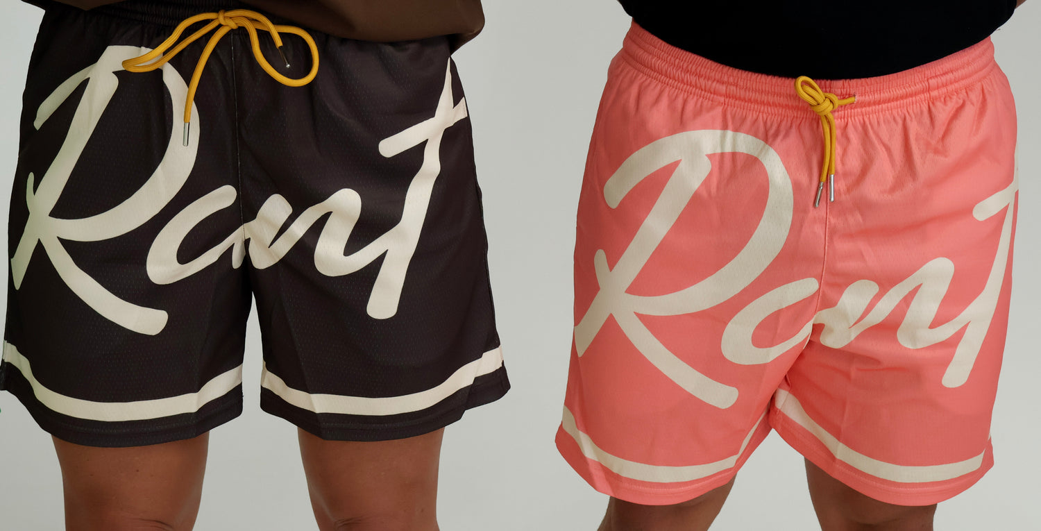 Two people wearing sporty mesh shorts, one dark brown and one coral pink, both with bold script lettering and yellow drawstrings.
