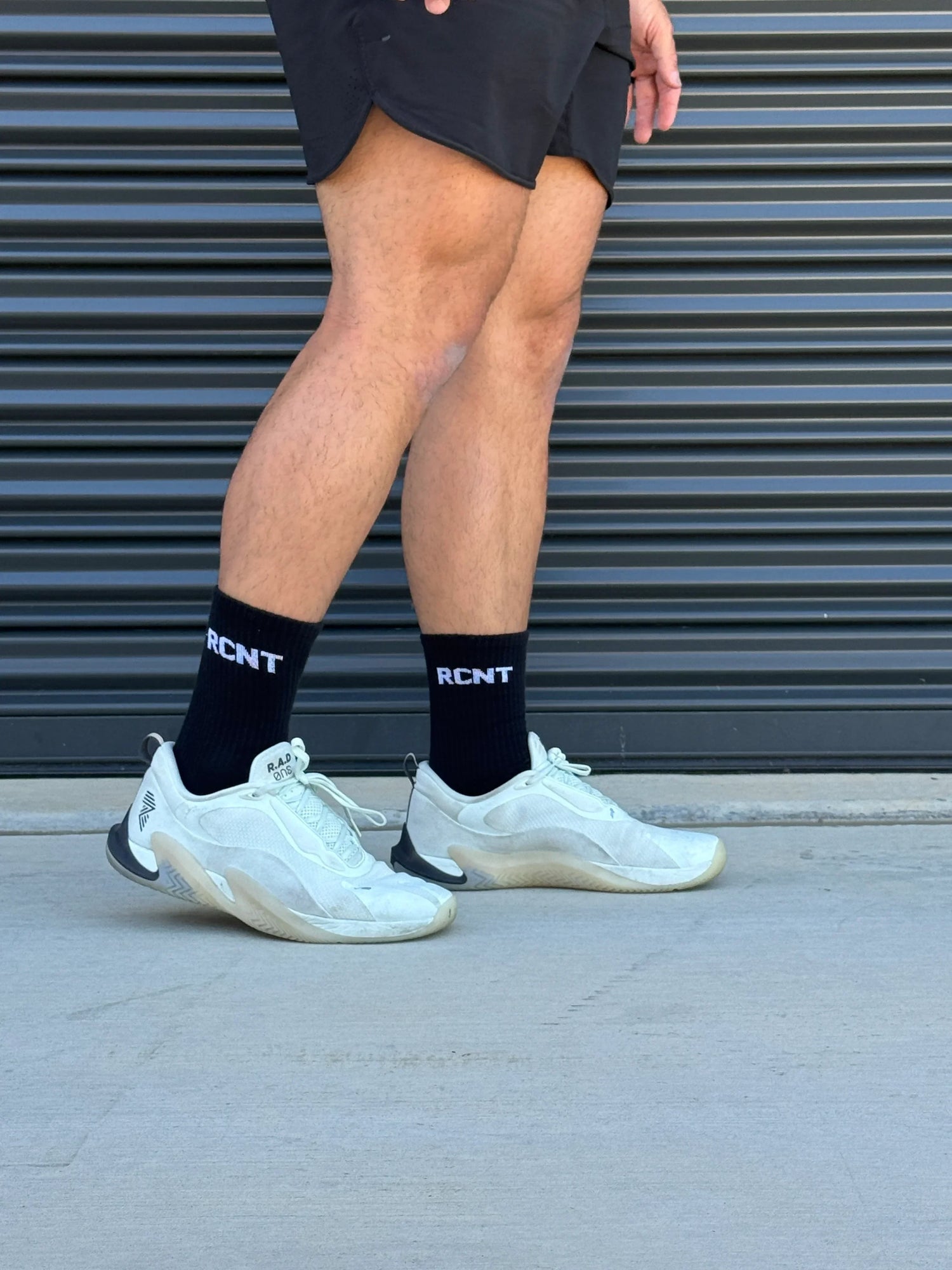 Athletic man in black shorts, black RCNT socks, and white sneakers standing outside