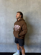 man in brown RCNT Grind Club hoodie, black shorts, white socks and sneakers against gray wall