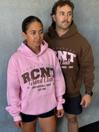 Two models wearing RCNT Grind Club hoodies in pink and brown against a gray wall