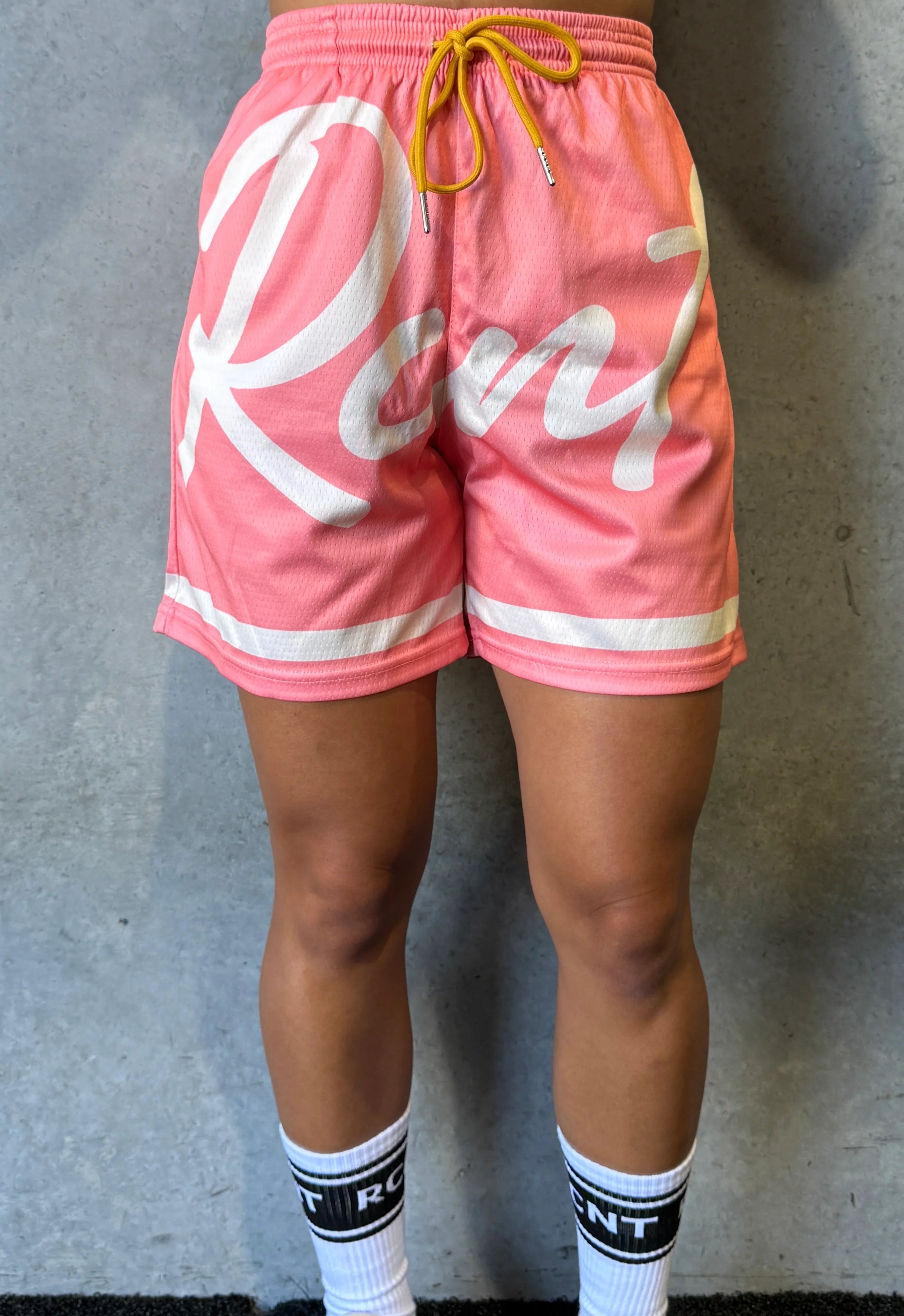 Person wearing pink sports shorts with white text and mustard yellow drawstring against gray wall