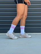 person wearing white athletic socks with pink RCNT text and beige sneakers against black corrugated wall