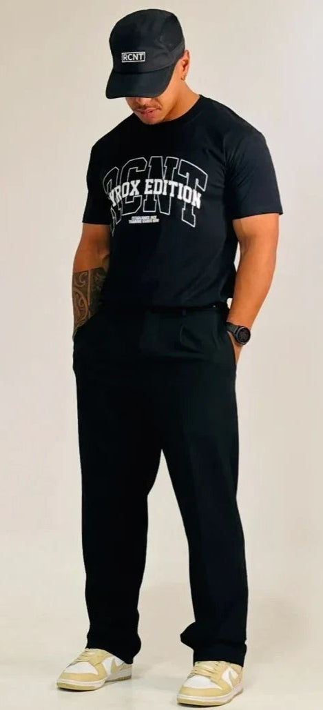Man wearing black RCNT cap, black RCNT ProX Edition t-shirt, black pants, and beige sneakers