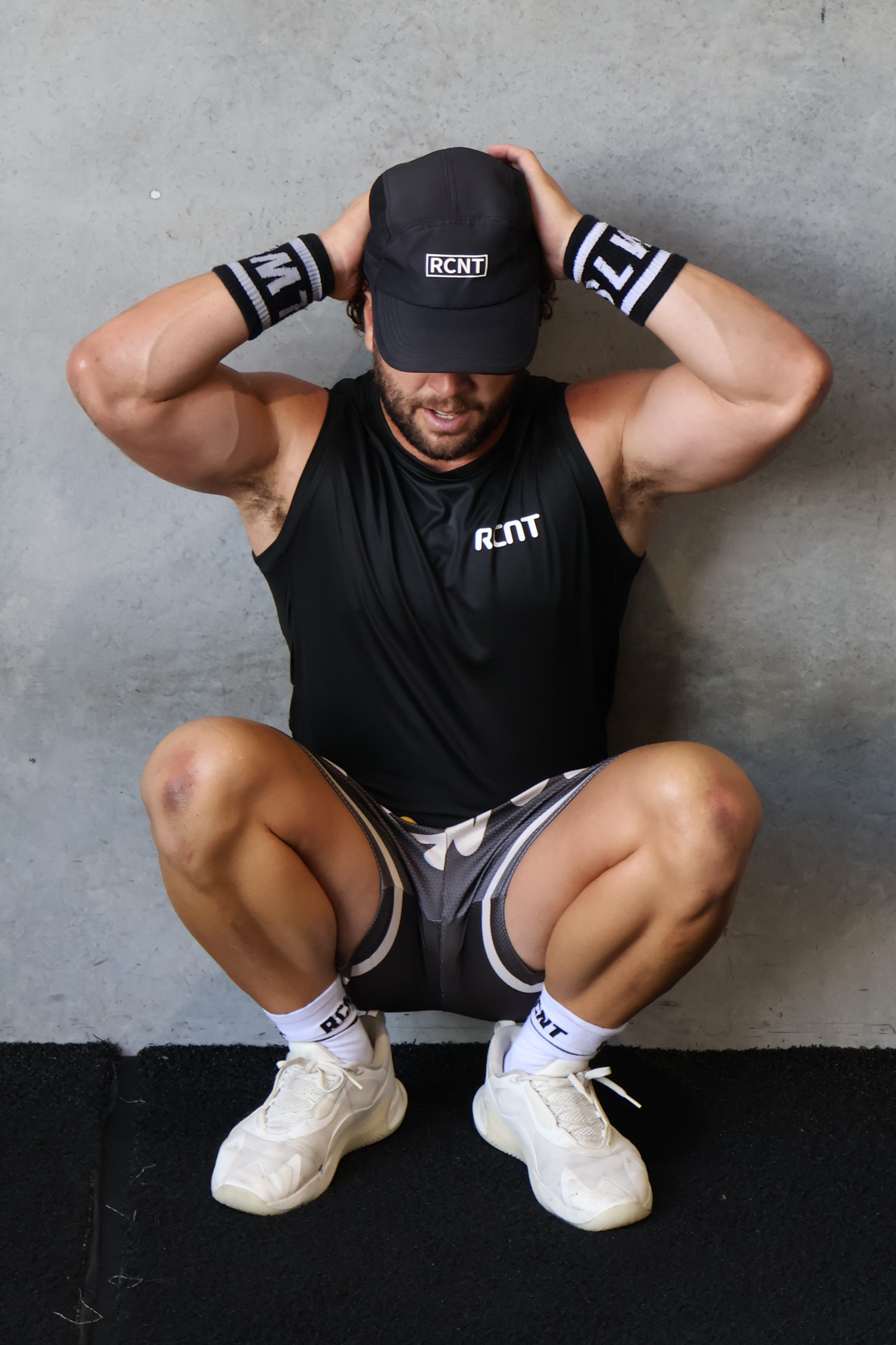 Person in athletic wear and cap sitting on the floor against a gray wall